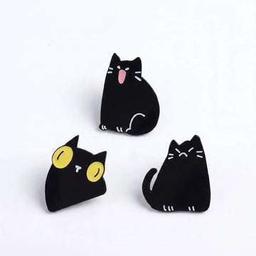 Three black cat enamel pins with shouting, wide-eyed and grumpy expressions